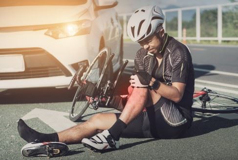 man laying on the ground after getting knocked off his bike by a car